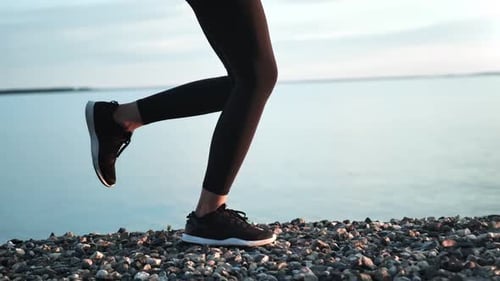 Female Legs in Sneakers and Sportswear Running on Pebbles at Beach
