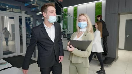 Young Confident Man and Woman in Coronavirus Face Masks Touching Elbows Greeting in Office Entrance