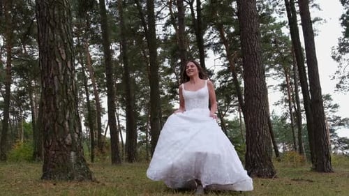 Happy Smiling Bride Runs Through the Woods Holding a Dress in Her Hands