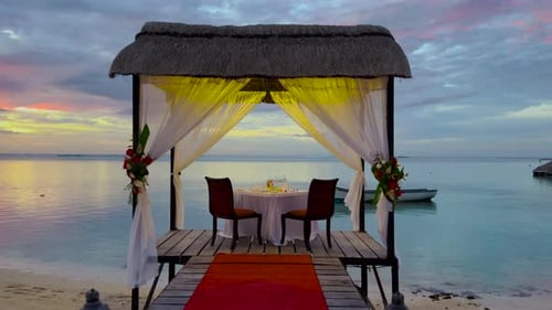 Romantic Evening Table for Two Persons on the Beach at Sunset on the Background of Beautiful Clouds