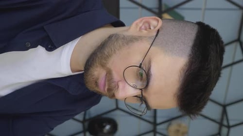 Vertical Video Close-Up Portrait Of A Young Male Freelancer with Glasses Working On An Online
