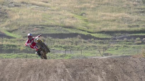 A young man riding his motocross dirt motorcycle off jumps.