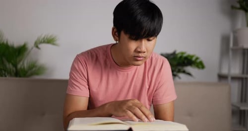 Man reading a textbook and sitting on couch in living room at home