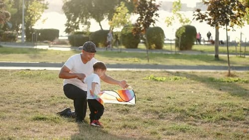 Father and Son Flying a Kite in City Park on Sunset