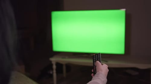 The girl is sitting in front of the TV in the evening with a remote control in her hand, chroma key