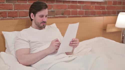 Man Lies in Bed Writing on Paper