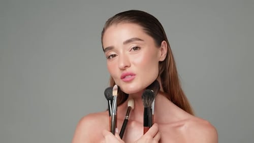 Woman Posing with Makeup Brushes in Studio