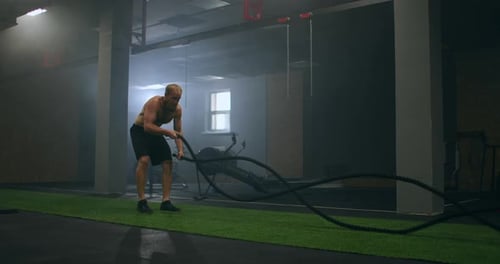 Fitness Man Exercising with Battle Rope Abandoned Warehouse. Tough Man Working Out in Cross Training
