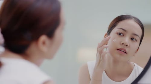 Woman Applying Moisturizer to Face in Mirror