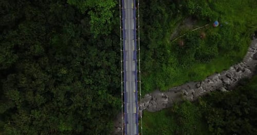 Aerial shot of metal suspension bridge build in the crossing of the valley and river with waterfall.