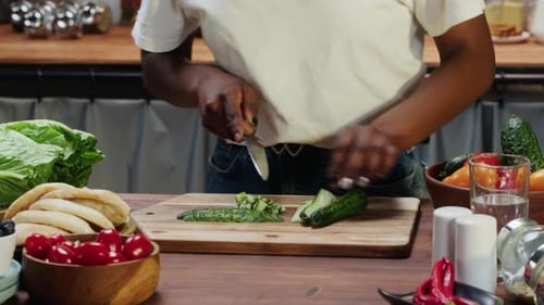 Person dicing cucumber on cutting board in kitchen