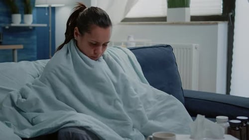 Personne atteinte de maladie qui a froid avec une couverture et un oreiller sur le canapé