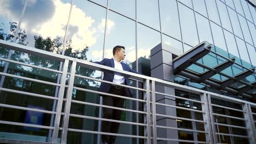 Confident young Asian businessman standing at the railing modern skyscraper office building