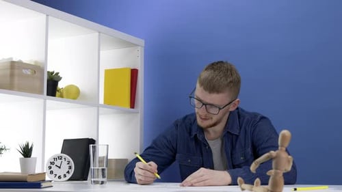 Young Man Drawing at Table with Wooden Mannequin
