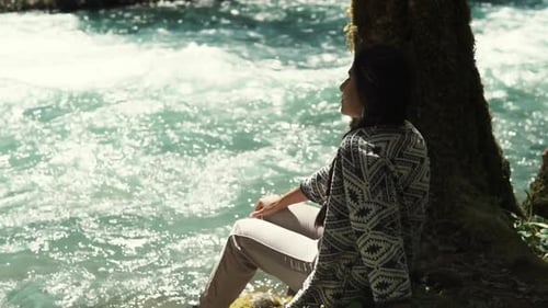 Frau, die im Park spazieren gegangen ist, sitzt in der Nähe eines Flusses und schaut auf das Wasser
