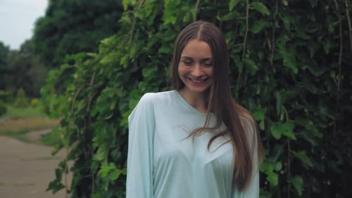 Attractive Girl Standing Near the Green Tree and Smiles, Straightens Hair