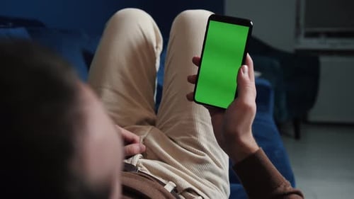 Man Lying on Couch Using Smart Phone with Chroma Key Green Screen at Night, Scrolling Through Social