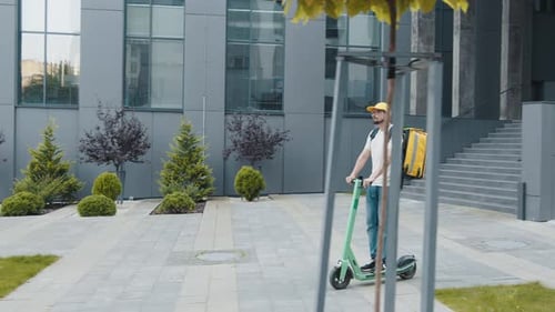 Repartidor barbudo con bolsa térmica o mochila montando un patinete eléctrico
