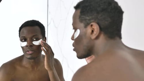 Man Applying Eye Patches in Mirror