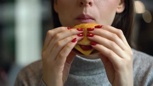 Woman Eats a Hamburger in a Cafe