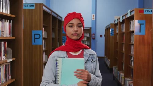 Porträt einer lächelnden asiatischen Studentin mit rotem Hijab, die in einer Bibliothek studiert