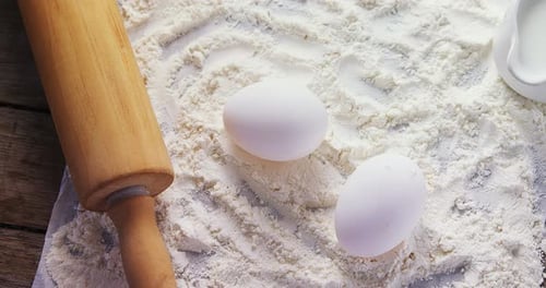 Flour, eggs and rolling pin placed over butter paper on a table 4k