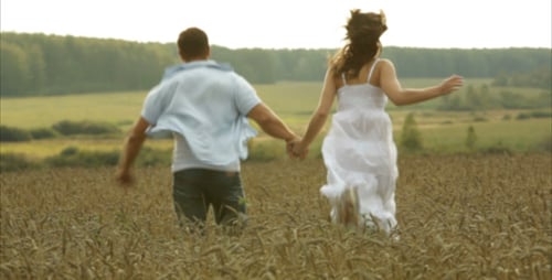 Couple Running Hand-in-Hand Through Wheat Field