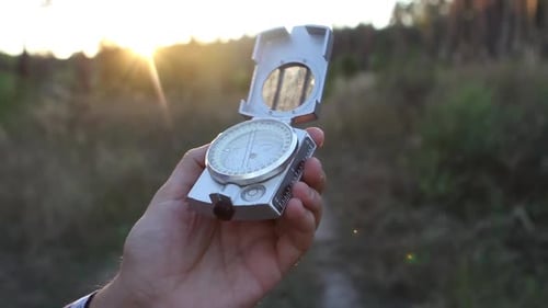 Man Uses a Compass In The Woods At Sunset