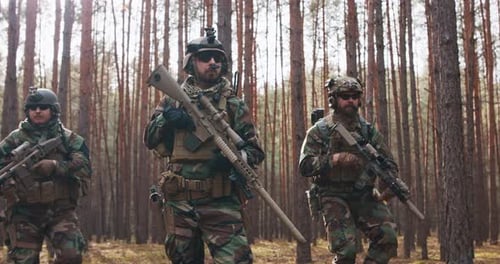 Quatro soldados de meia idade totalmente equipados em uniformes de camuflagem formam uma linha pronta para disparar mirando