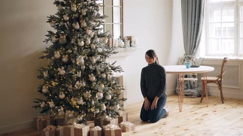 Woman Arranges Christmas Presents Under Decorated Tree