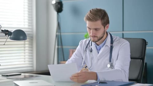 Doctor Using Smartphone While Working on Laptop in Clinic