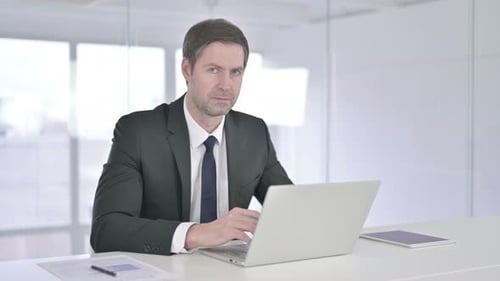 Fröhlicher Geschäftsmann mittleren Alters zeigt mit dem Finger in die Kamera