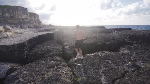Man Jogging on Rocky Terrain Along Ocean
