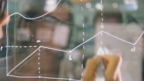 Young Attractive Female Office Worker Writing on Glass Whiteboard Close Up