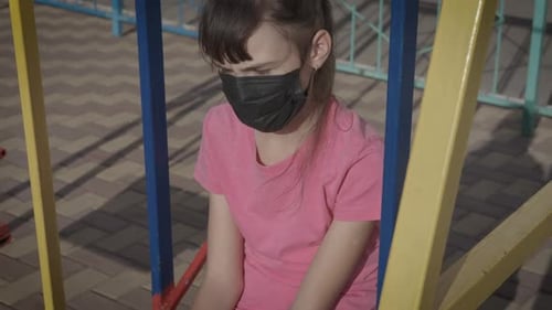 Child Wearing Mask Sits Alone on Swing