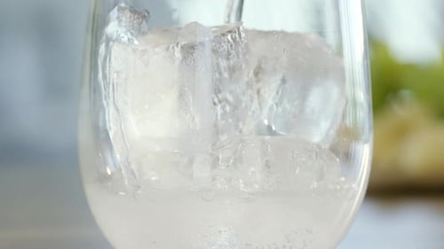 Bubbly Liquid Pouring Over Ice in Glass
