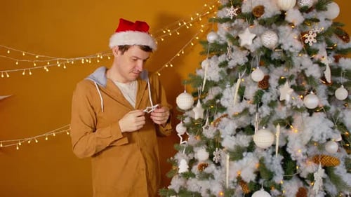 Man Decorates Christmas Tree with Baubles and Lights