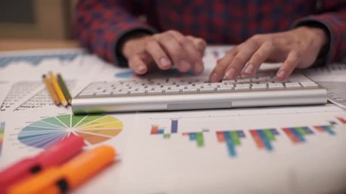 Hands Typing Keyboard Amongst Charts and Graphs