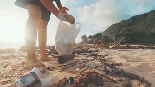 Young Caucasian Woman Volunteer Collects Debris From Ocean Sand Puts It in Bag