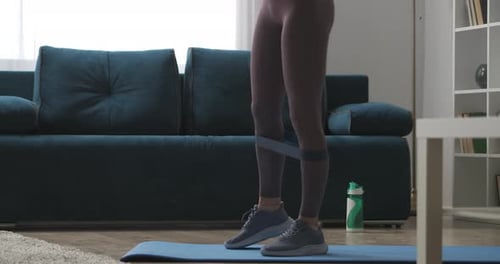 Home Fitness Woman Is Training Legs with Sporty Elastic Band Tensing Muscles Closeup View in Living