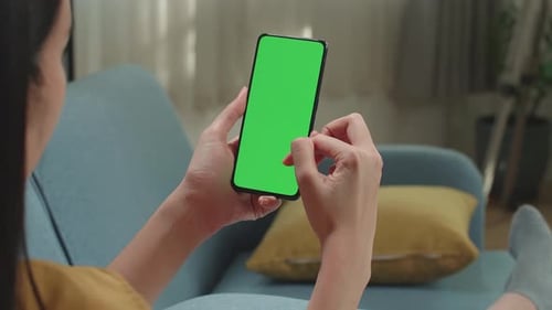 Woman Sitting On Couch In Living Room Using Smartphone With Mock Up Green Screen Display