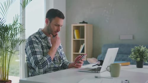 Young Adult Man Uses Smartphone at Desk