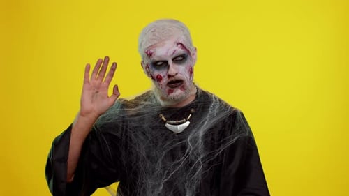 Homem zumbi assustador de Halloween sorrindo, amigável, acenando com as mãos gesticulando olá ou adeus, dando boas-vindas