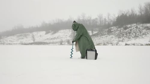 Mann mit Eisbohrmaschine in den Händen auf gefrorenem Eissee im Winter