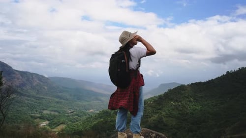 Backpacking female hiker stands on top of the mountain and enjoying the view.