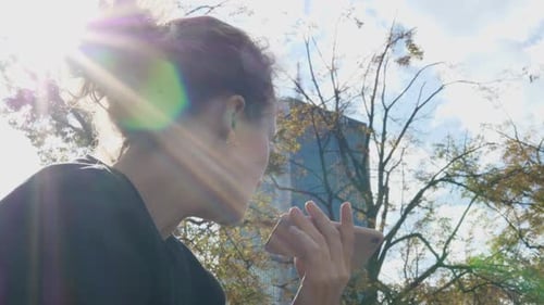 Woman Recording Voice Message on the Smartphone on a Sunny Day at the Park