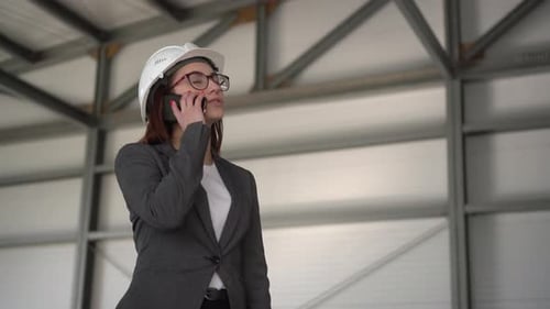 Woman in Hard Hat Talking on Smartphone Indoors