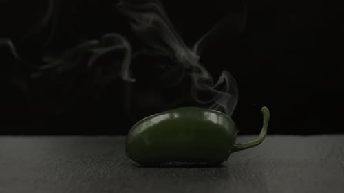 Green jalapeño chili pepper with smoke effect on black background