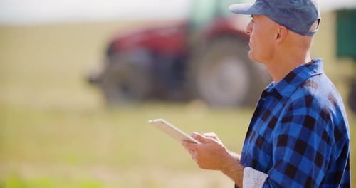 Farmer Using Digital Tablet While Looking at Tractor in Farm