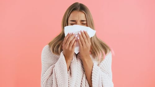Young Woman Blowing Nose with Tissue on Pink
